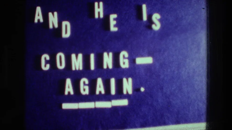 1976 Athens home-movie title card on a blue background with spaced white letters reading AND HE IS COMING-AGAIN.