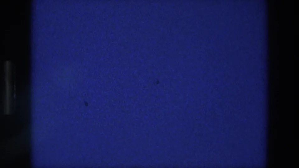 Blue 8mm film frame from the 1976 Athens reel, showing grain, faint flicker, and dark vertical borders.