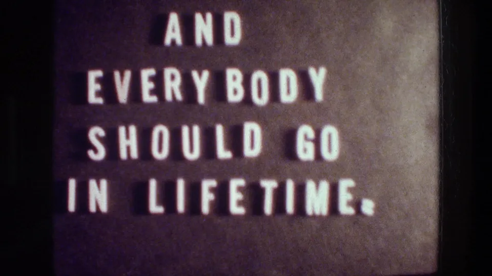 1976 Athens 8mm frame showing white block letters on a dark board with the phrase ending in “IN LIFETIME.”
