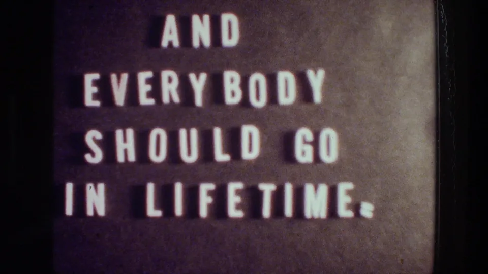 1976 Athens 8mm frame of a dark letterboard-style sign reading “AND EVERYBODY SHOULD GO IN LIFETIME.”