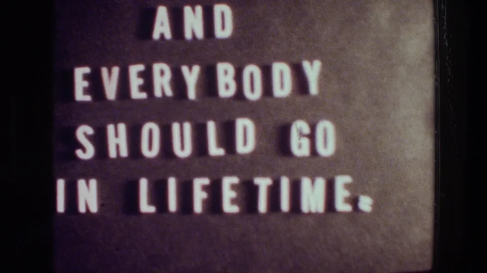 1976 Athens 8mm frame showing the same white-letter phrase on a dark board, with visible grain and soft focus.