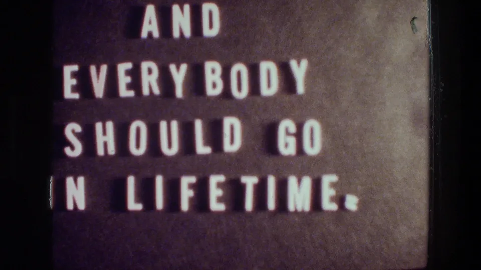 1976 Athens 8mm close-up of white letterboard text, partly cropped by the frame, with blue color occupying the lower half.