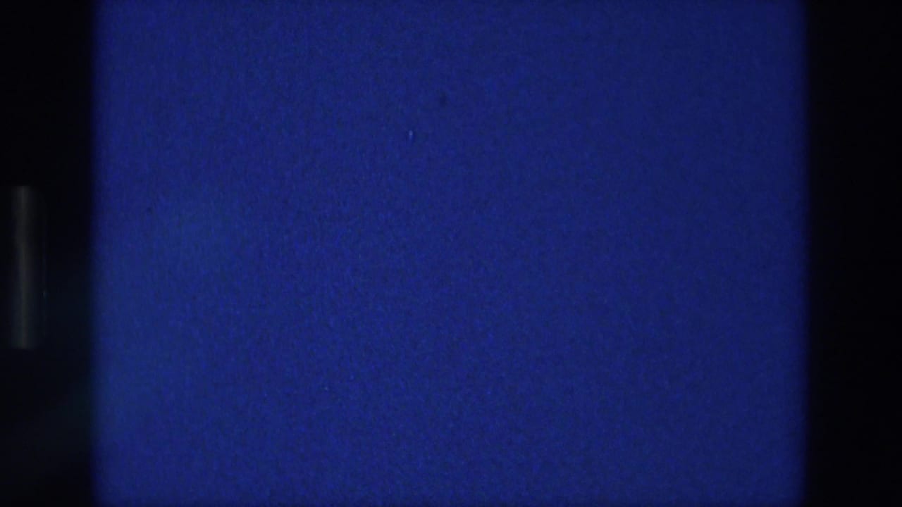 1976 Athens home-movie frame showing a blue exposed field with black film borders, grain, and small dust specks.