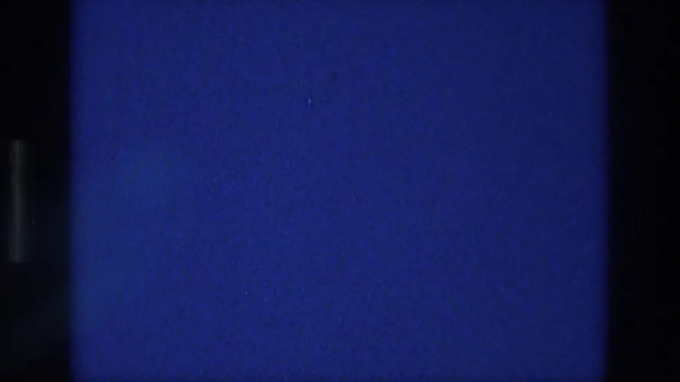 1976 Athens home-movie frame showing a blue exposed field with black film borders, grain, and small dust specks.