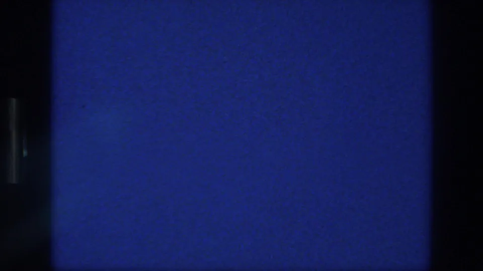 Final blue frame from the 1976 Athens 8mm clip, showing black borders, grain, and a faint frame-line division.