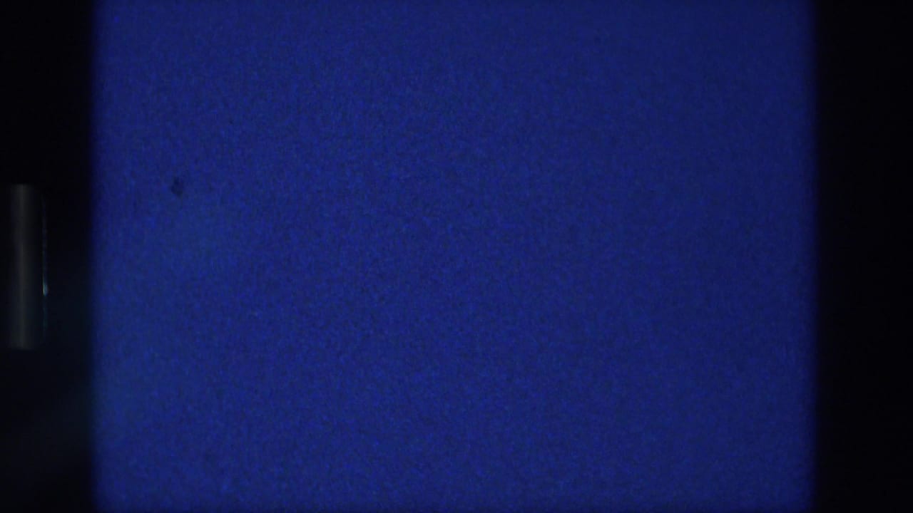 1976 Athens home-movie frame showing a deep blue sky field with faint cloud haze, grain, dust specks, and dark scan borders.