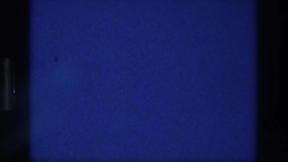 1976 Athens home-movie frame showing a deep blue sky field with faint cloud haze, grain, dust specks, and dark scan borders.