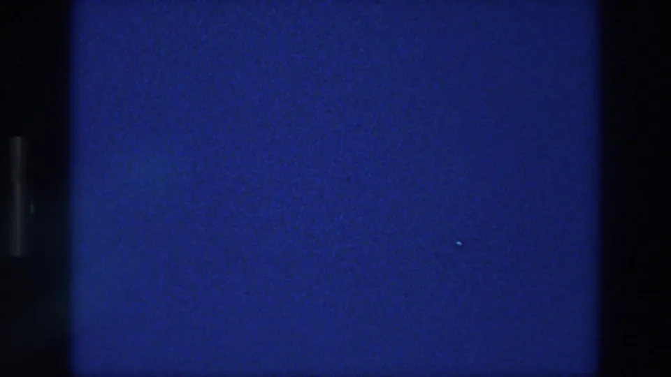 1976 Athens 8mm frame with open blue sky, visible grain, a tiny bright speck, and dark scan borders along the contact sheet.