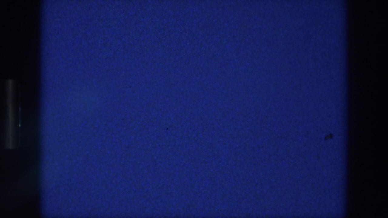 1976 Athens 8mm frame showing a blank deep blue field with visible film grain, slight vignetting, and dark frame separation at the sides.
