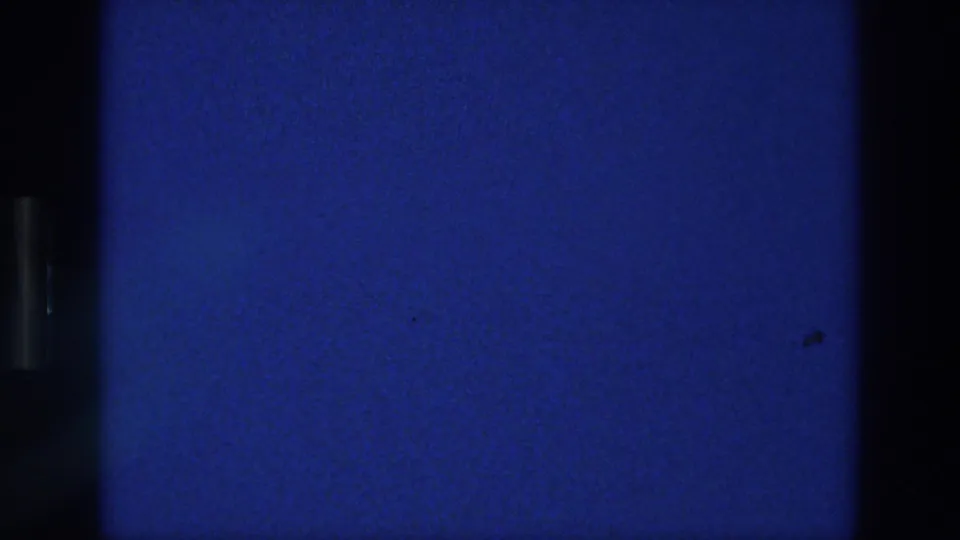 1976 Athens 8mm frame showing a blank deep blue field with visible film grain, slight vignetting, and dark frame separation at the sides.