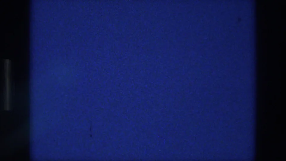 1976 Athens 8mm frame showing a blank blue field with subtle film grain, minor specks, a faint horizontal seam, and dark side borders.