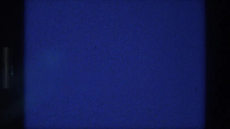 1976 Athens 8mm frame showing a deep blue exposed field, black frame-edge shadow, grain, and faint specks.