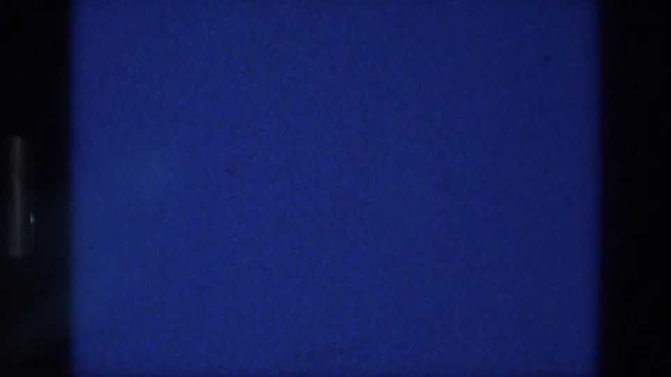 1976 Athens 8mm frame with deep blue color, dark frame-edge shadow, visible grain, and scattered dust specks.