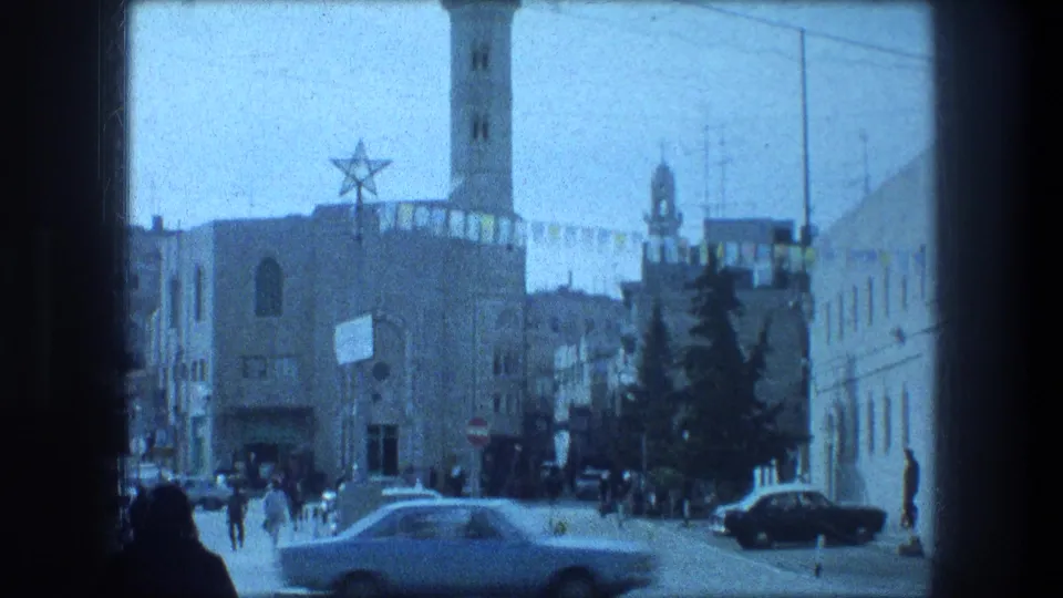 Bethlehem street scene from 1976 with pedestrians, cars, overhead wires, and a star-topped building with a tower.