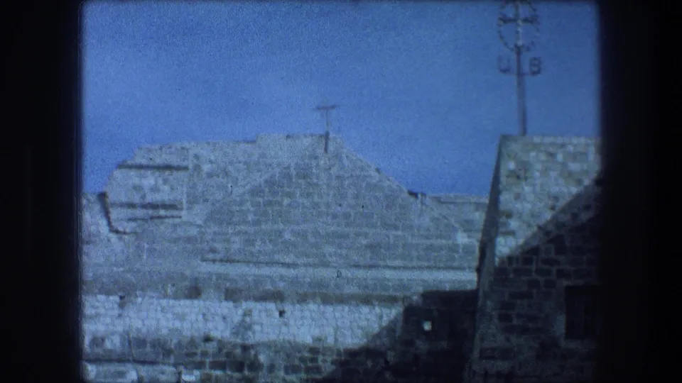 1976 Bethlehem architectural cutaway showing weathered stone walls, a low roofline, small dark window, and a utility or light pole overhead.