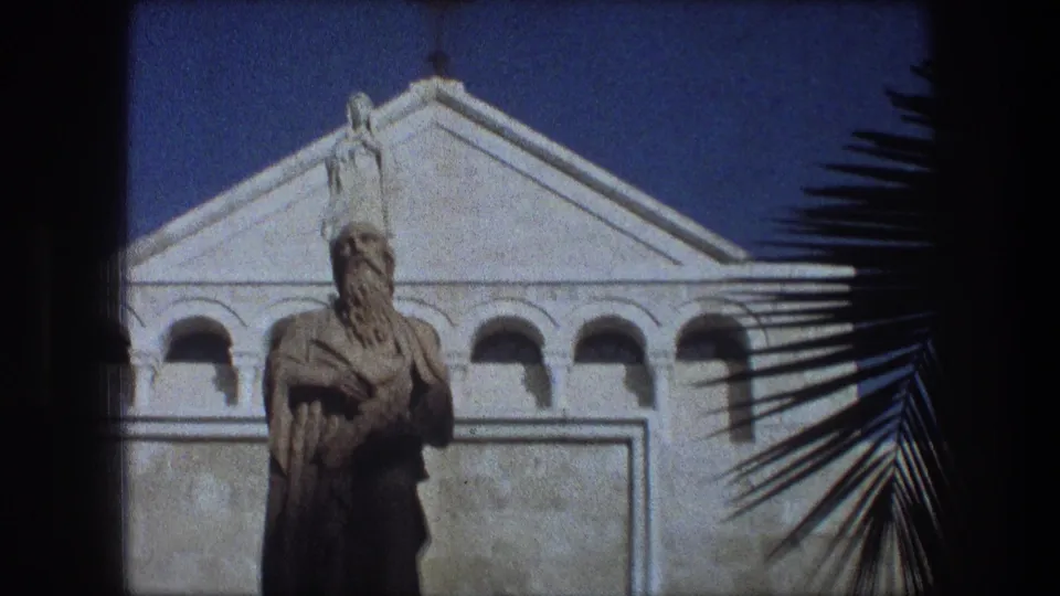 1976 Bethlehem 8mm frame showing a bearded statue on a pedestal in front of a pale facade with arches and a cross.