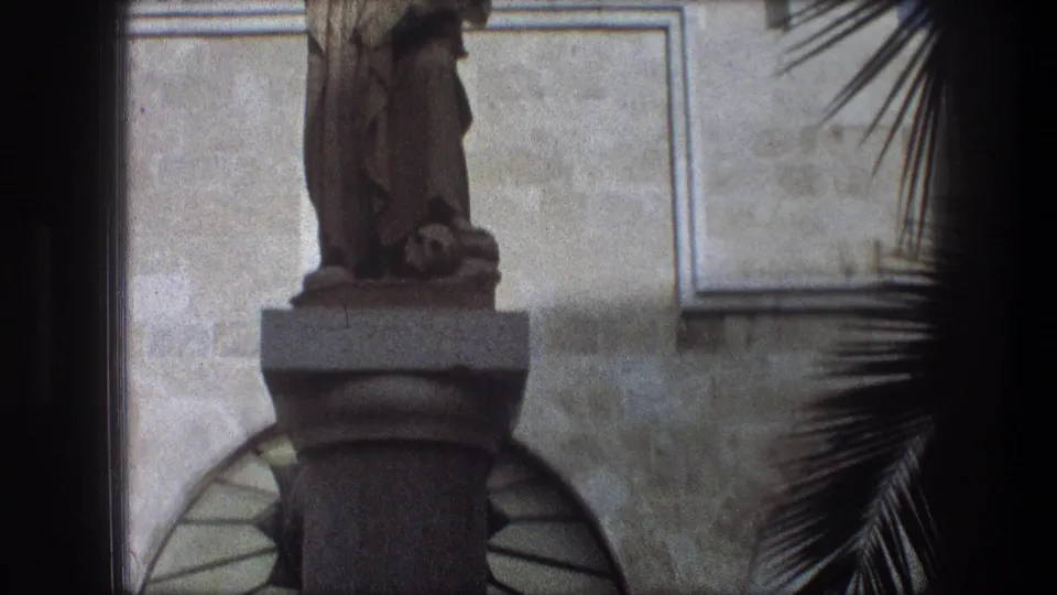 Closer 1976 Bethlehem frame showing the lower statue, pedestal, arched doorway area, and palm fronds at right.