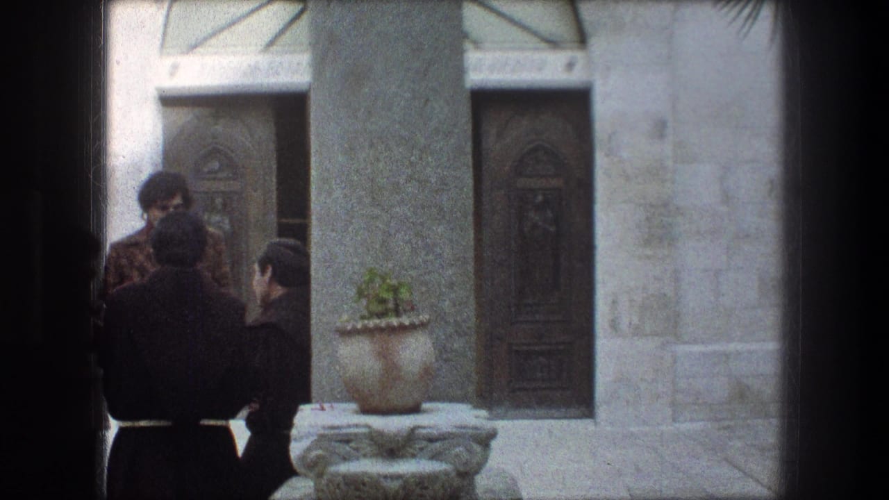 Three robed men stand beside a column and potted plant outside carved doors.