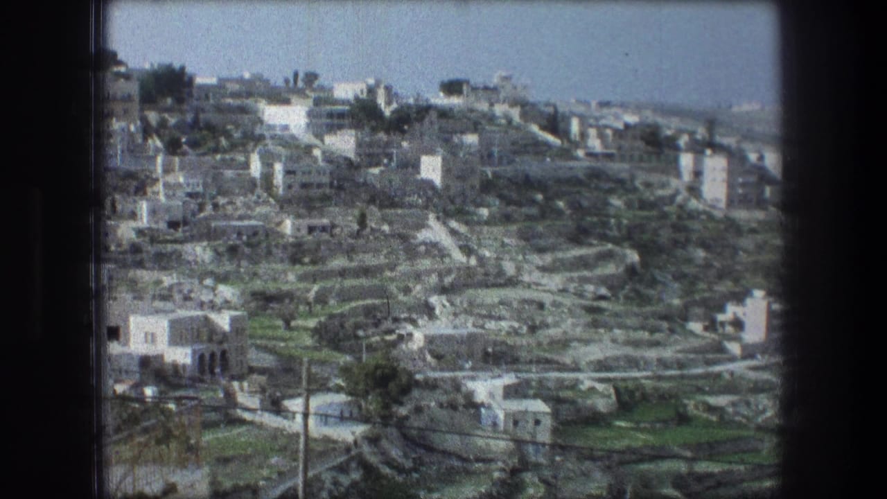 Wide hillside townscape with clustered pale buildings, terraces, roads, and distant skyline.