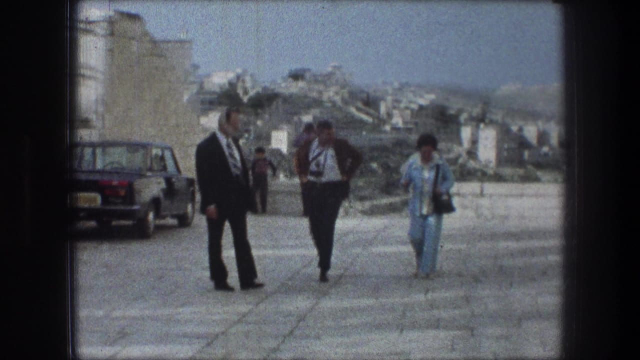 Three adults walk along a pale stone pathway beside a parked dark sedan.