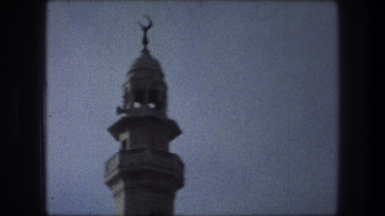 Closer view of a minaret top and crescent finial against blue sky.