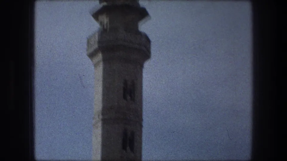 1976 Bethlehem home-movie frame showing the minaret shaft and upper tower from a low angle, softened by film grain.