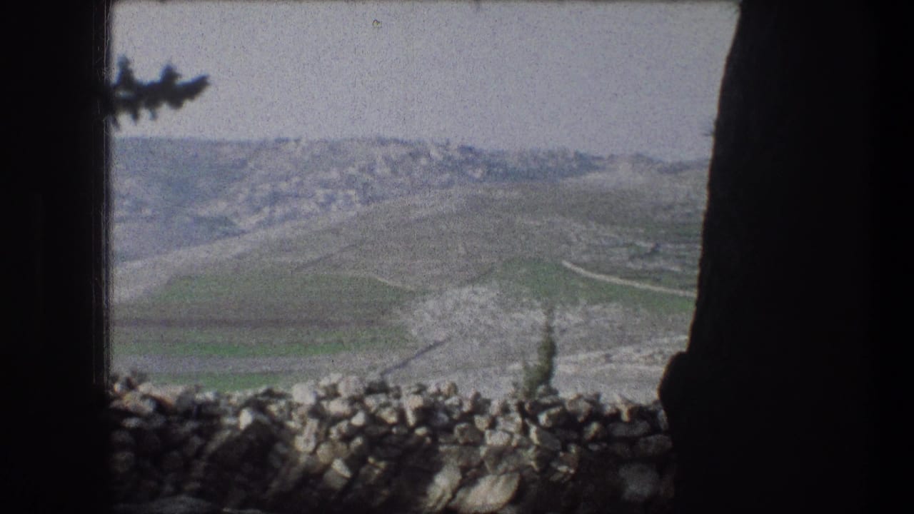 Rolling hillside seen past a stone wall and dark window-like frame edges.