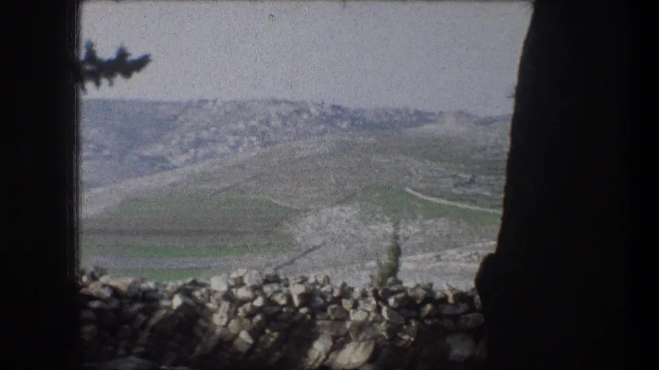 1976 8mm view near Bethlehem showing rolling green hills beyond a low stone wall, framed by dark foreground edges.