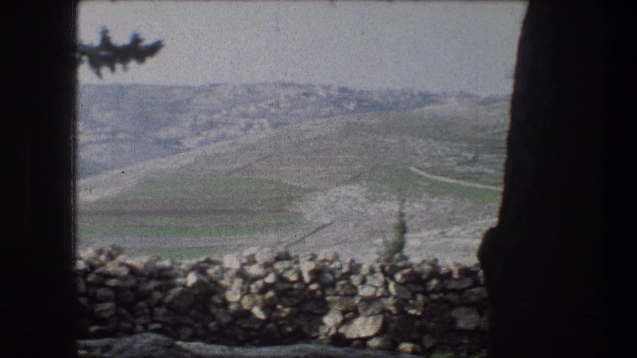 1976 8mm frame of Bethlehem-area hills with a low stone wall in the foreground and distant clustered buildings on the ridge.