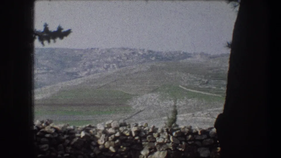 1976 8mm view near Bethlehem showing muted hills, green field patches, a low stone wall, and dark foreground framing.