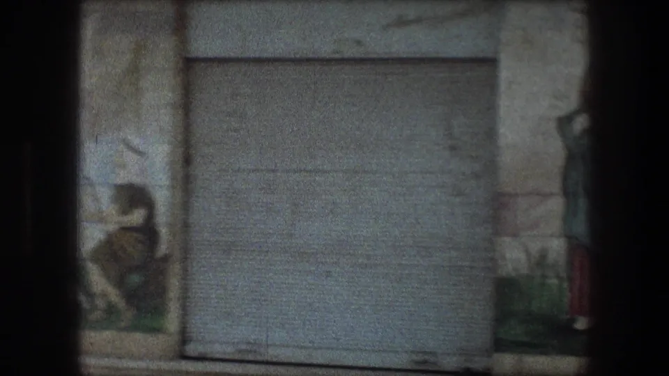 A gray metal door is centered between partial religious mural figures and painted sheep in the Bethlehem 8mm footage.