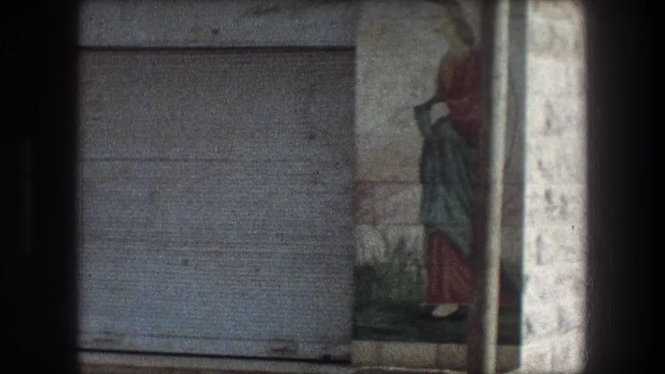 1976 Bethlehem 8mm frame showing a painted wall figure near a closed metal door and rough stone building surface.