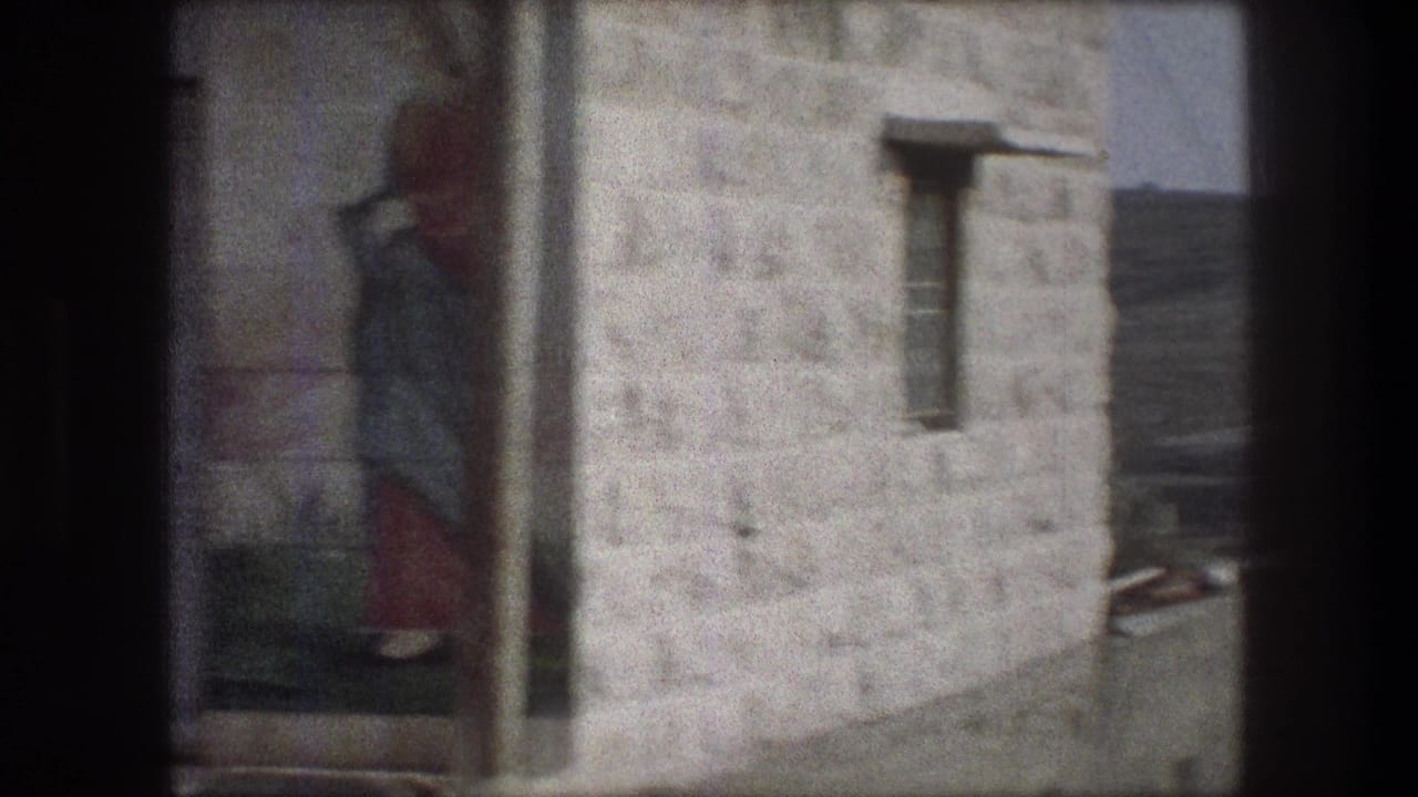 Bethlehem home-movie frame with a painted figure on a stone wall, a small window, and part of a roofline beyond.