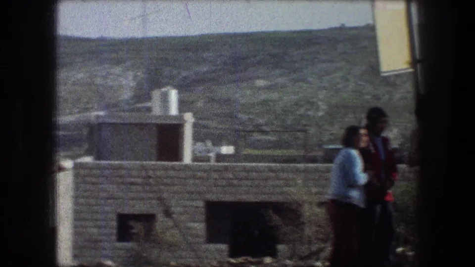 1976 Bethlehem 8mm frame showing two young people in casual clothing near stone buildings with rolling hills behind them.