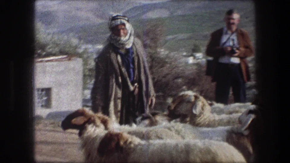 A shepherd in a grey coat stands among sheep, with a small white building and hillside visible in the 1976 Bethlehem scene.