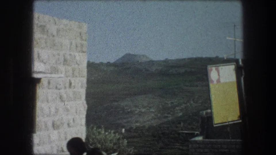 The final frame shifts to a Bethlehem rural landscape with a pale stone wall, distant hills, a signboard, and a partial person at the lower edge.