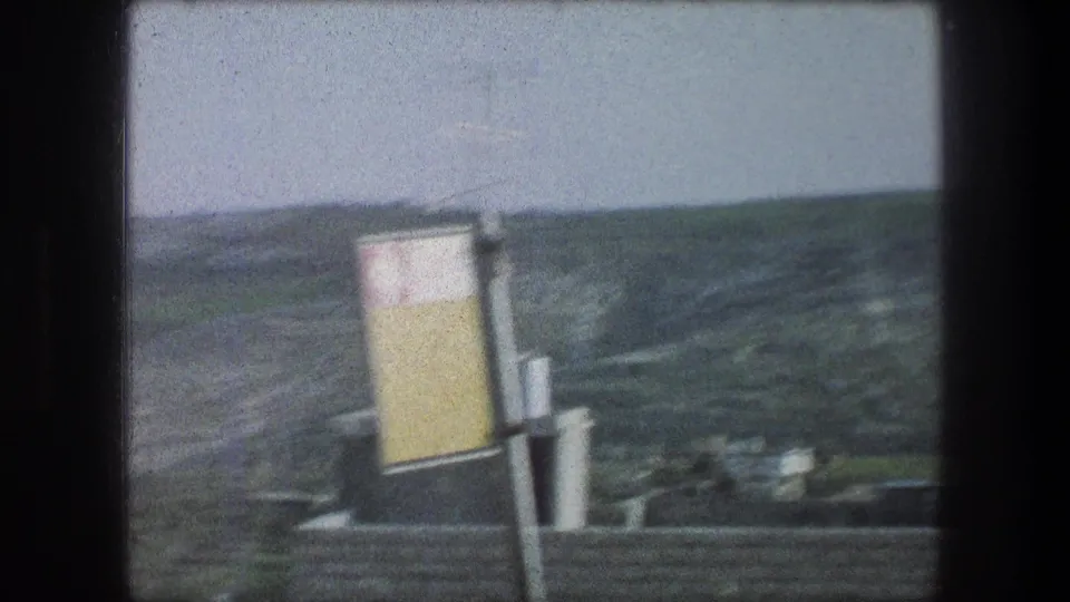 1976 Bethlehem hillside scene with a yellow-and-white sign, rooftops, chimney or vent pipes, and green slopes beyond.