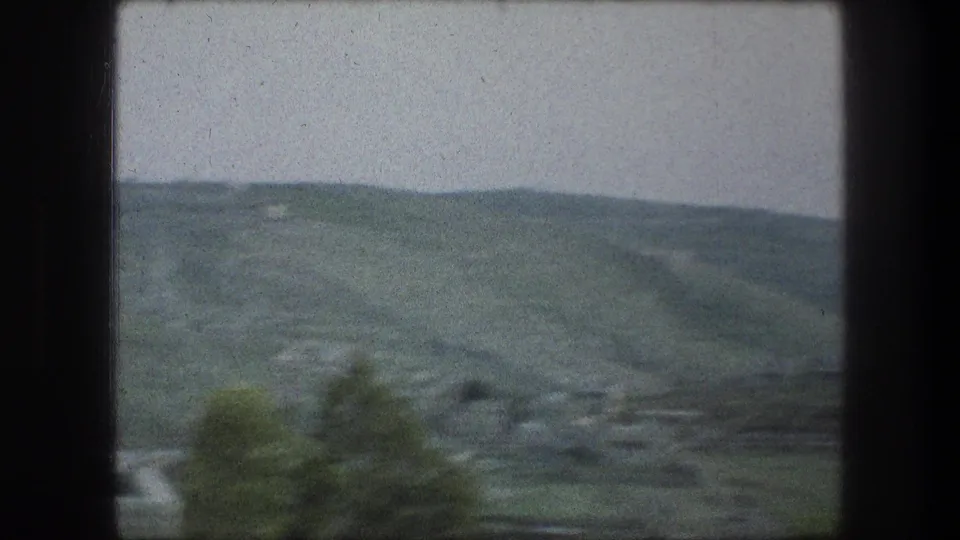 1976 Bethlehem landscape frame showing open green hillside, scattered buildings, trees, and rooftops from a moving 8mm pan.