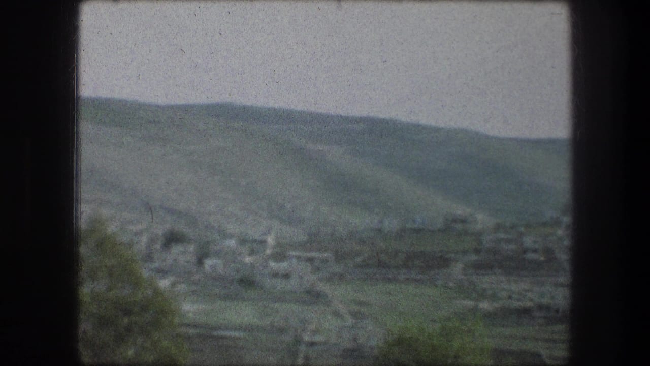 Soft distant view of green hills and a valley settlement through a dark 8mm frame border.