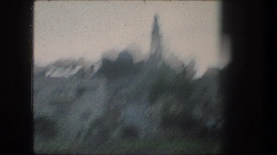 Soft 1976 8mm view of Bethlehem with pale buildings, a domed roofline, and a tall church-like tower beyond dark window framing.
