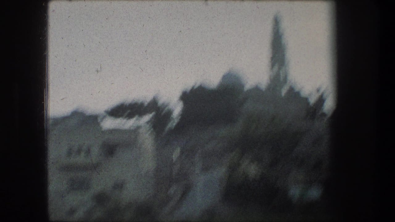 Bethlehem skyline in soft focus, with pale stone buildings, a rounded dome, and a narrow tower seen from inside a dark window frame.