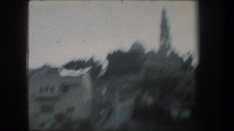 Bethlehem skyline in soft focus, with pale stone buildings, a rounded dome, and a narrow tower seen from inside a dark window frame.