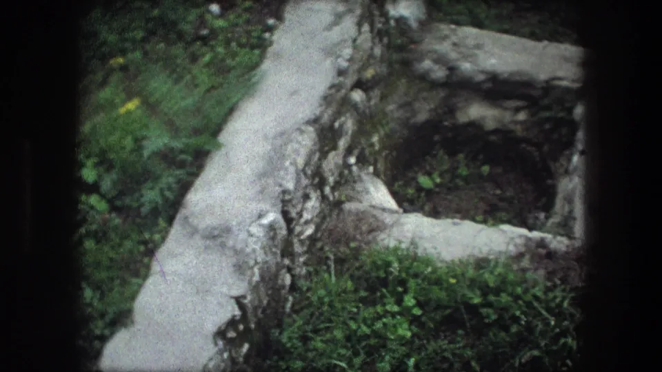 1976 Bethlehem 8mm frame showing a rectangular stone pit or opening with grass, dirt, and aged masonry around it.