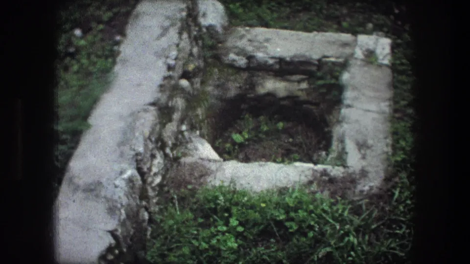 1976 Bethlehem 8mm frame with a weathered rectangular stone pit, pale stone edge, grass, and soil.