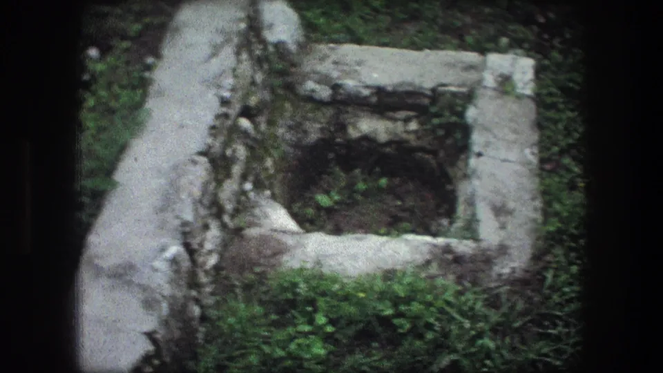 1976 8mm Bethlehem footage showing a weathered stone well-like structure surrounded by moss, grass, and low masonry.