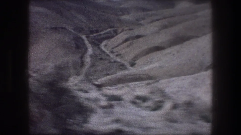 1970s 8mm travel footage frames a dry Bethlehem valley with sloped hills and a winding pale channel below.