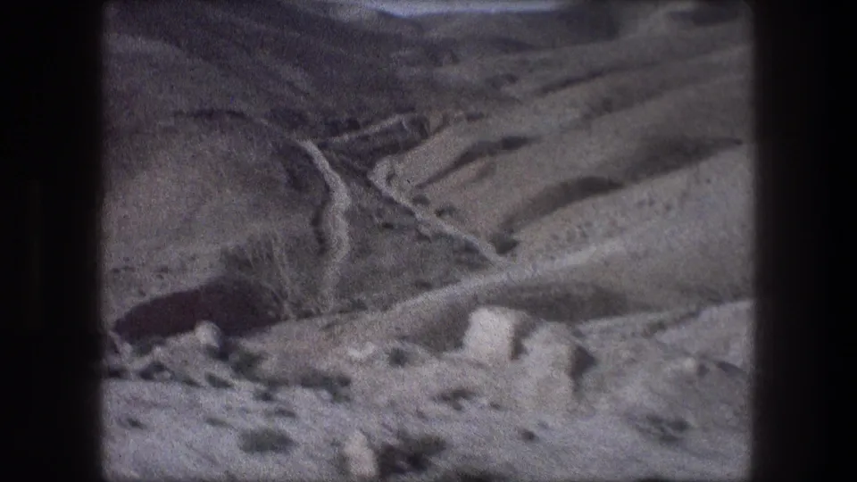 1976 8mm view near Bethlehem showing a pale dirt road winding through arid, rocky mountain terrain.