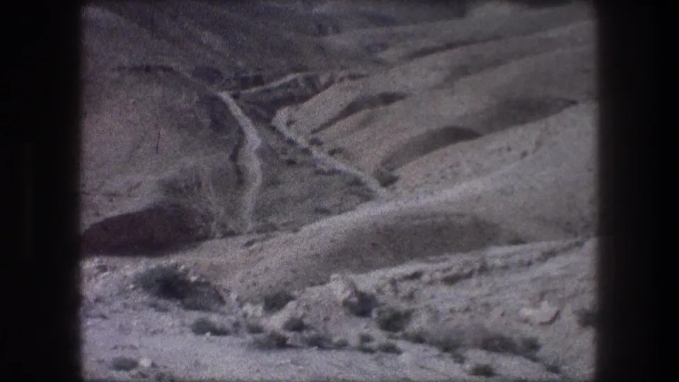 1976 8mm frame near Bethlehem showing a dry mountain valley crossed by a winding dirt road.