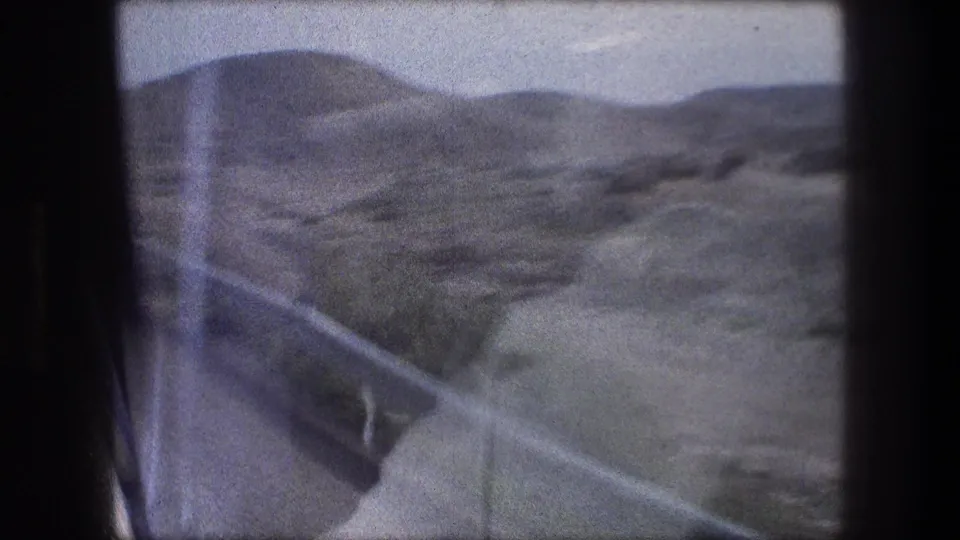 Vehicle-window view near Bethlehem with a roadside guardrail, paved edge, and dry hills receding into haze.
