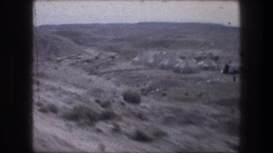 1976 Bethlehem-area home-movie frame with a dirt road, scattered tent-like shelters, scrub, and low barren hills.